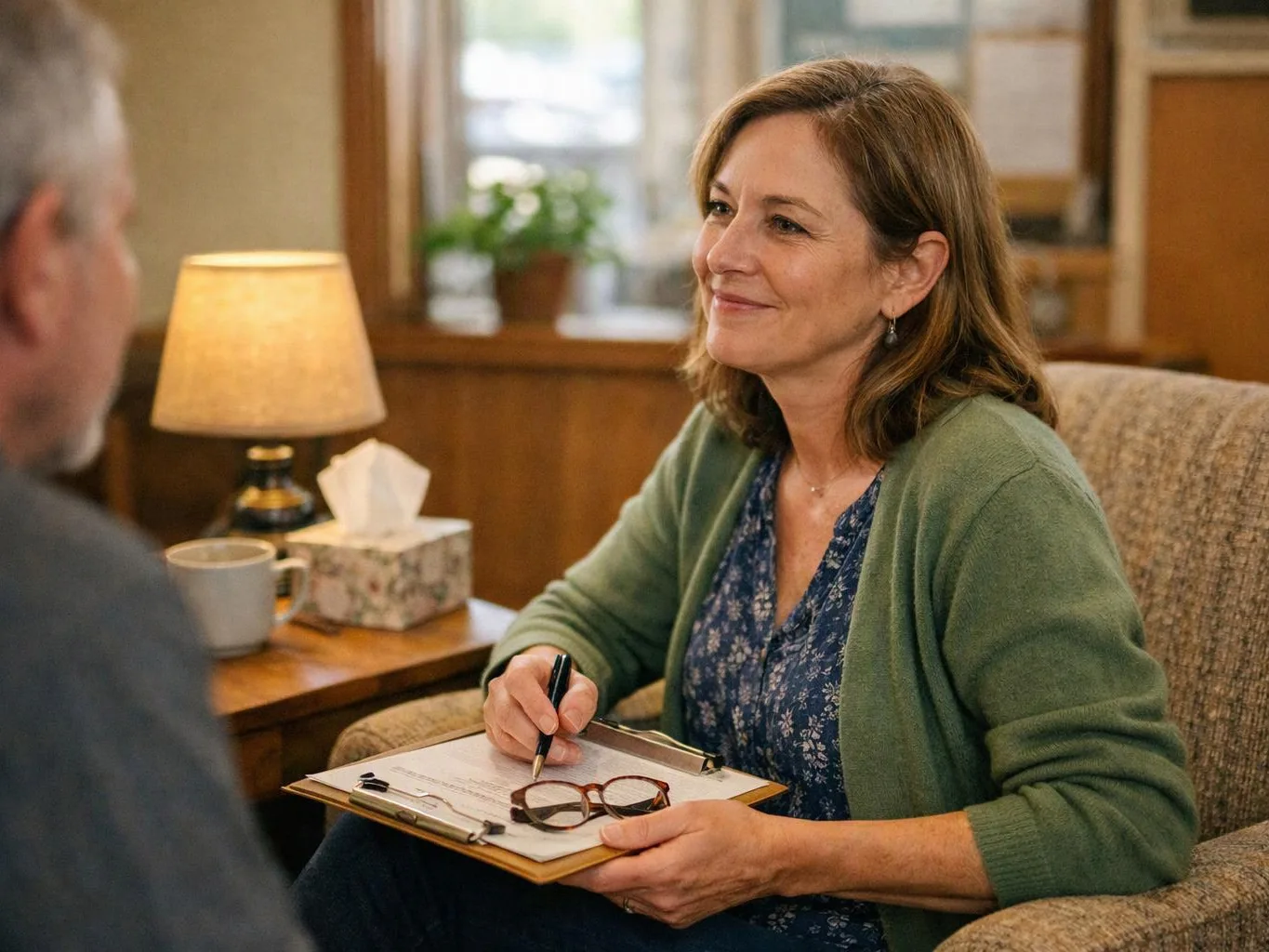 A smiling woman takes notes on a clipboard during a seated conversation in a cozy office room