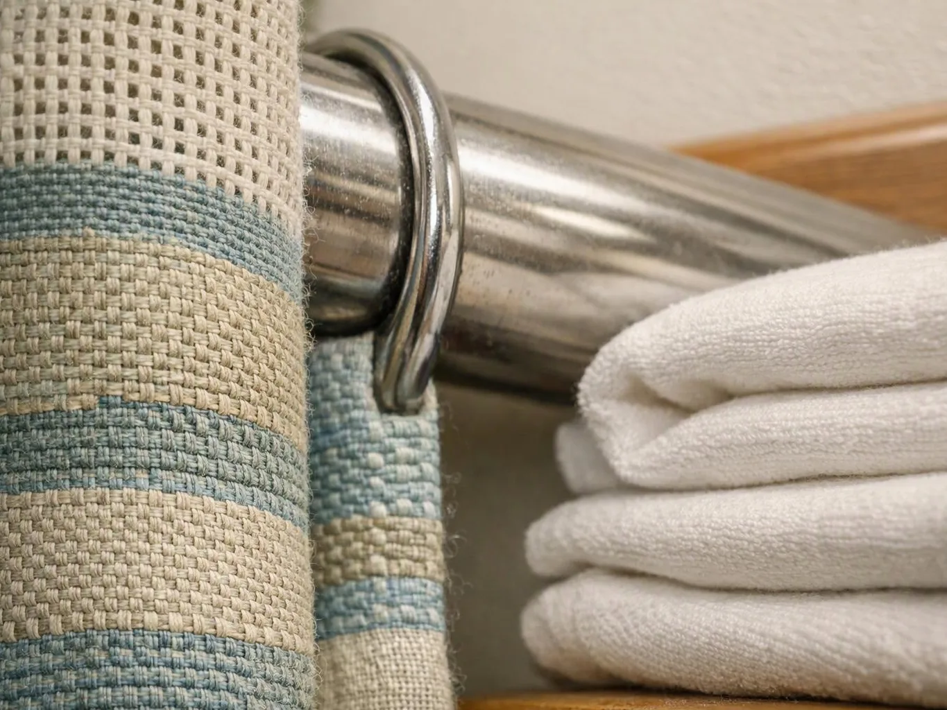 Striped fabric and folded white towels hang on a chrome rod in a bathroom setting